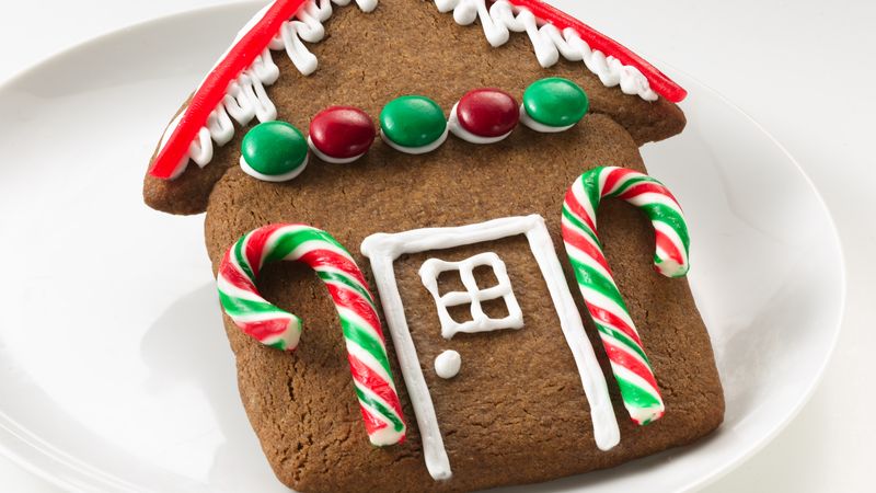 House-shaped gingerbread panel baked flat on a plate, decorated with piped icing windows and candy canes