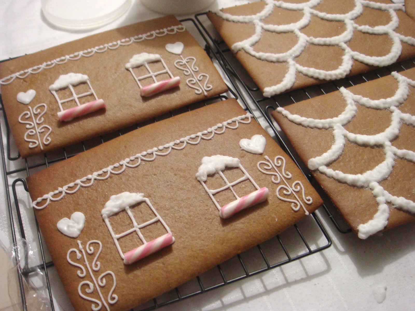 Baked gingerbread wall and roof panels cooling on a wire rack, decorated flat with piped white icing before the house is assembled