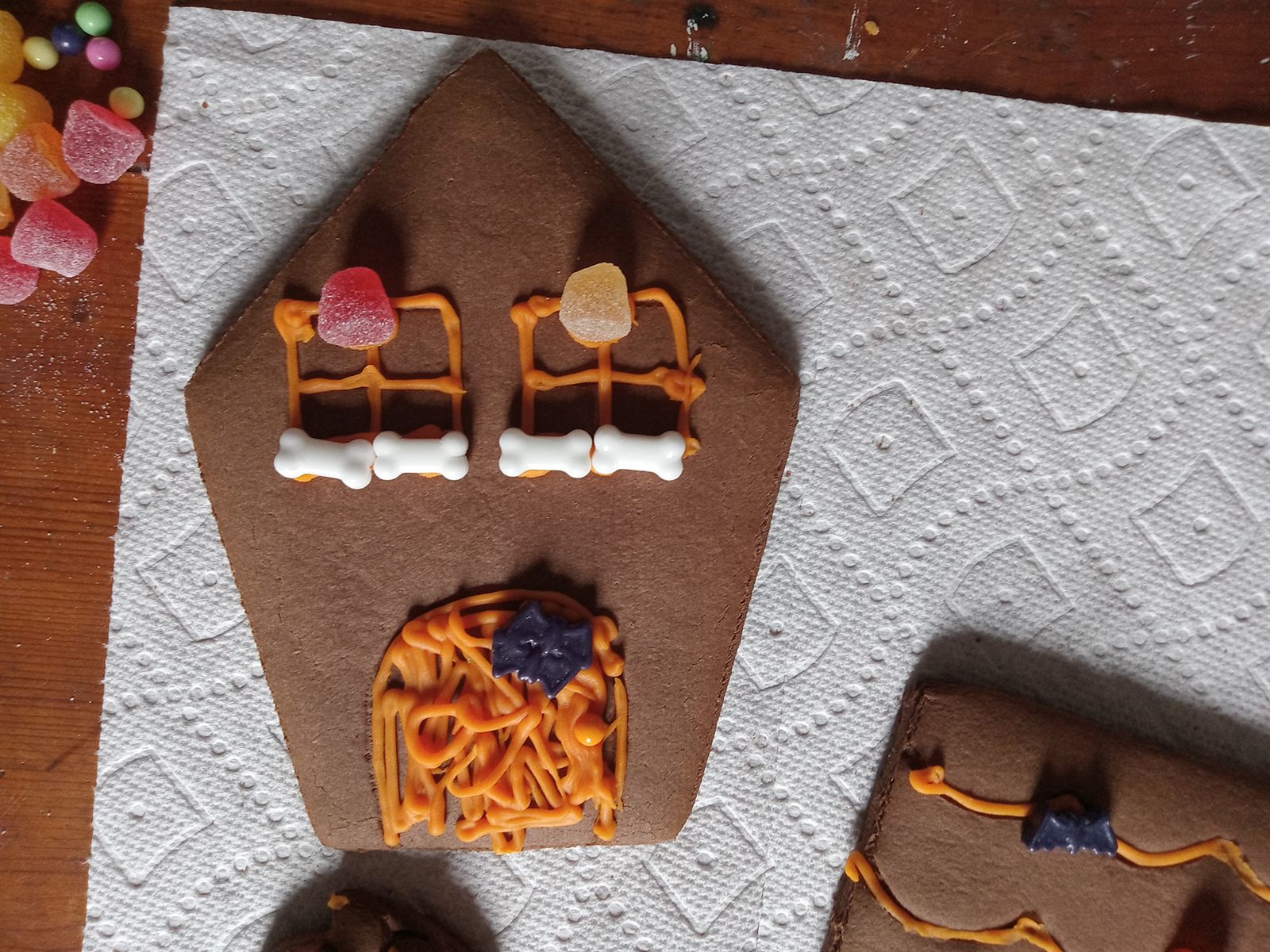 flat gingerbread wall panel decorated with orange piped windows, white bone sprinkles and a purple bat before assembly